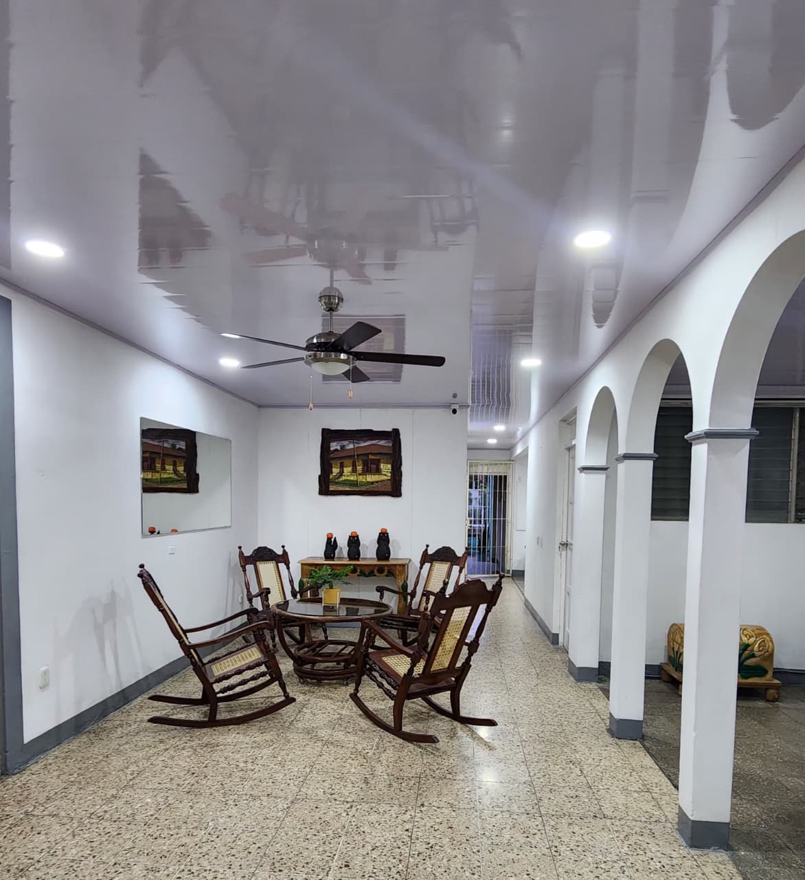 Sala de Casa Cordero con mecedoras de madera, mesa de vidrio y corredor de arcos