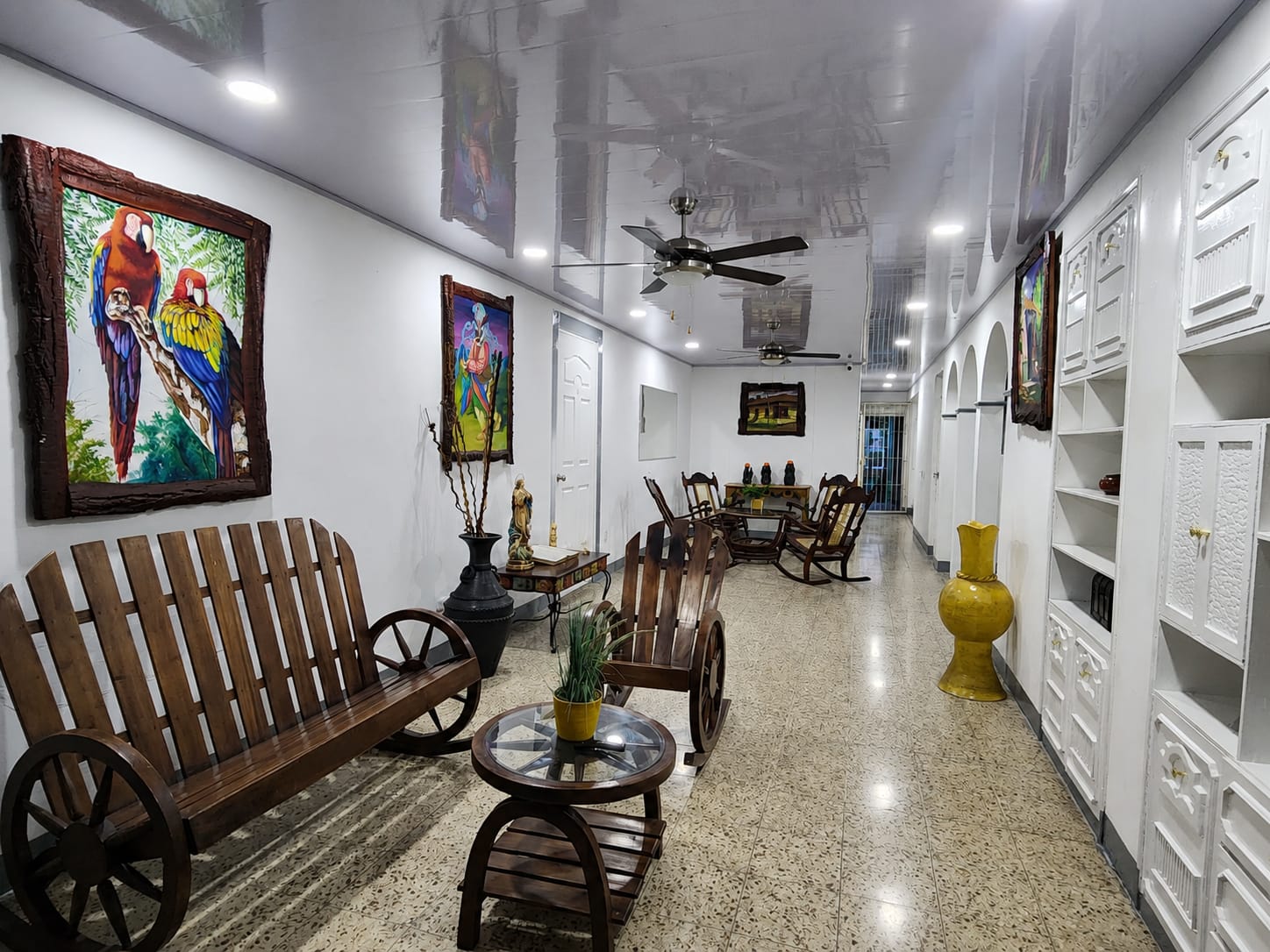 Sala con banca de rueda de carreta, cuadro de guacamayas y estantería blanca